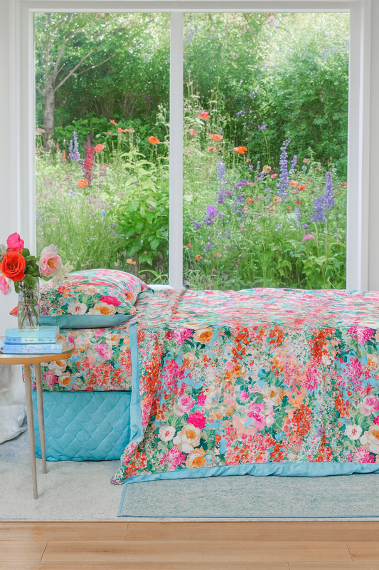bộ chăn ga cotton cao cấp hoạ tiết hoa nhí phối hoa hồng góc chụp từ bên cạnh chiếu vaò chăn phủ trên đệm chạm xuống dưới sàn, mầu hoa tươi sáng rực rỡ, cửa kính nhìn ra. bên ngoài khu vườn